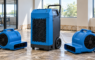 Close-up of a blue commercial dehumidifier flanked by two air movers in an office undergoing water damage restoration.